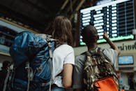 Two backpackers checking the digital board at a train station for travel information.