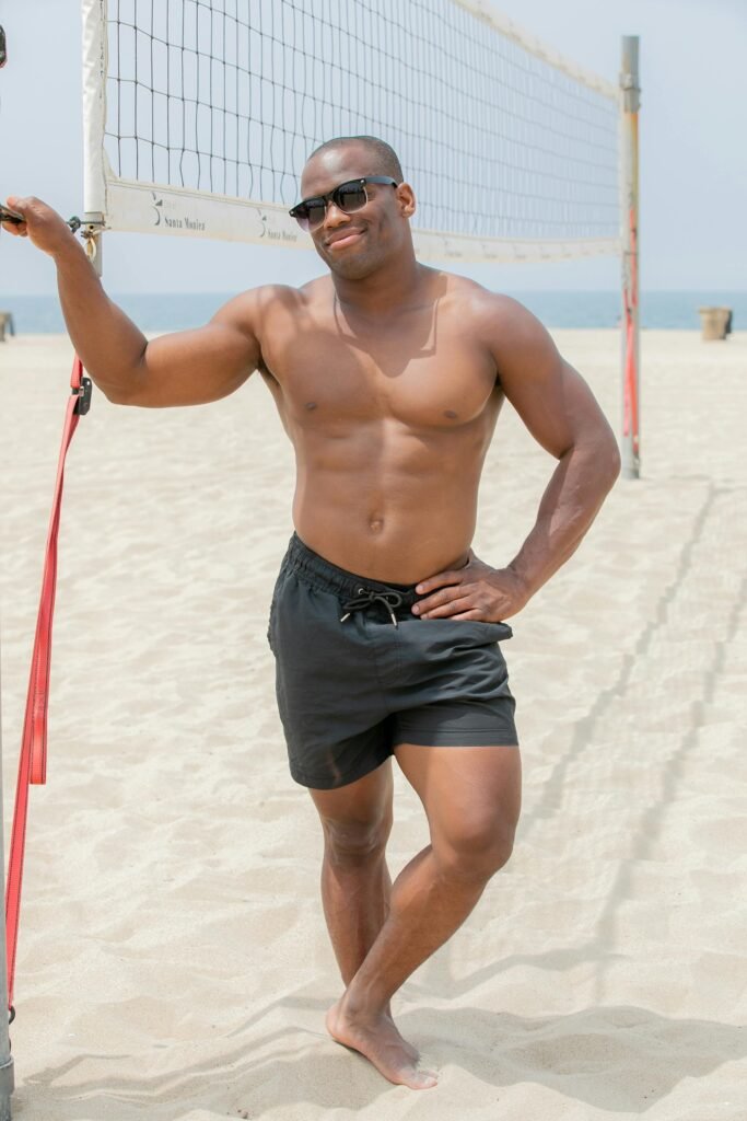 pexels-photo-12169354-12169354 Shirtless man standing by a volleyball net on the beach, enjoying a sunny day.