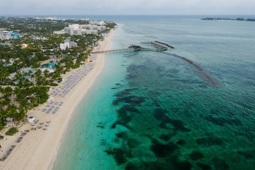 A tranquil aerial view of a beachfront resort, white sandy beach, and an extensive pier stretching into the turquoise sea.