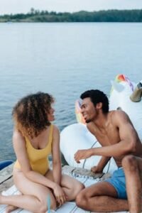A cheerful couple enjoys a sunny day by the lake, sitting on a dock with inflatable floats.